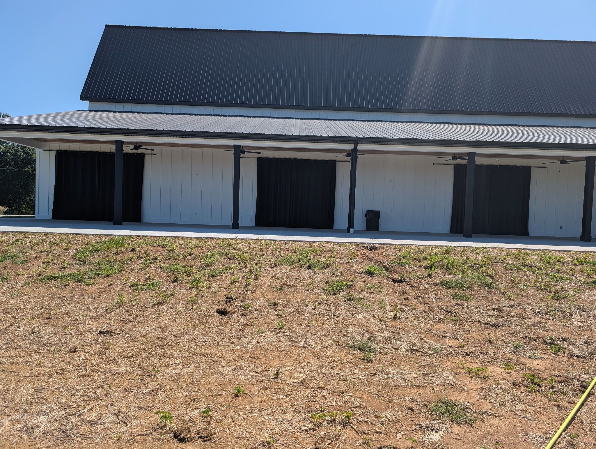 Um edifício com telhado plano, grandes portas pretas e uma área externa coberta.