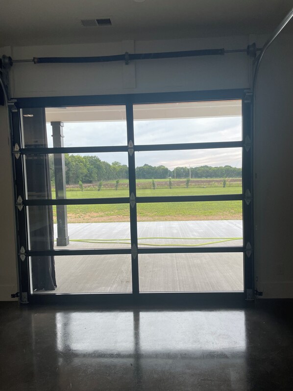 A garage door with a view of a green field and trees.