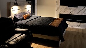 Un dormitorio moderno con cama, cómoda, televisor montado en la pared y una pared de acento de mármol.
