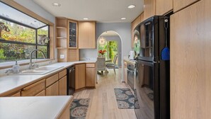 A modern kitchen with wooden cabinets, a black refrigerator, and a window overlooking greenery. - Quiet Riverside Retreat 3bd/2ba (Auburn)