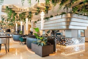 Un moderno vestíbulo de hotel con un mostrador de recepción curvo, zonas de estar y una escalera con vegetación.