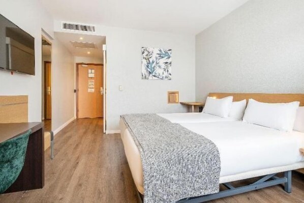 Una habitación de hotel con cama, mesita de noche y televisor en la pared.