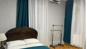 A bedroom with a wooden bed, white and blue bedding, a nightstand with a lamp, and a window with white curtains. - Tranquil bed & breakfast with AC in Zugdidi (Zugdidi)