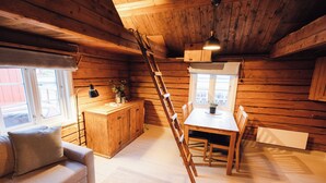 Interior acogedor de una cabaña con detalles de madera, una mesa de comedor con sillas, un sofá, una escalera y un ventanal con vistas.