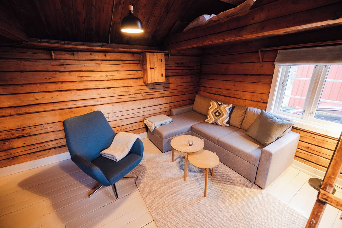 A cozy cabin interior with a blue armchair, grey sofa, and a small wooden table.