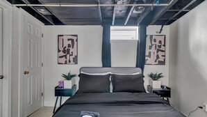 Une chambre à coucher moderne avec un lit noir, des murs blancs et des œuvres d’art abstraites accrochées aux murs.