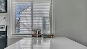 Une cuisine avec un plan de travail blanc, une fenêtre avec des stores et quelques boîtes de produits posées sur le plan de travail.
