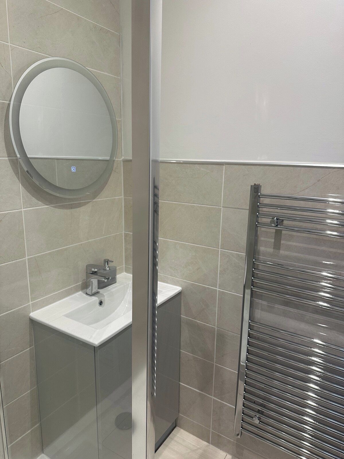 Un baño moderno con un espejo redondo, un lavabo y una cabina de ducha de vidrio.
