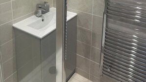 A modern bathroom with a round mirror, a sink, and a glass shower enclosure. - El Murrino Apartments 1 -Central (Bournemouth)