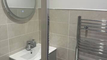 Un baño moderno con un espejo redondo, un lavabo y una cabina de ducha de vidrio.