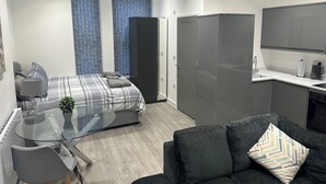 A modern bedroom with a glass table, a sofa, a bed with a grey and white checkered duvet, and a wardrobe. - El Murrino Apartments 1 -Central (Bournemouth)