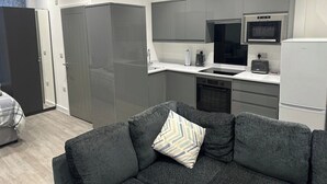 A modern kitchen with grey cabinets, a built-in oven, and a toaster. There is a grey sofa with a patterned pillow in the foreground. - El Murrino Apartments 1 -Central (Bournemouth)