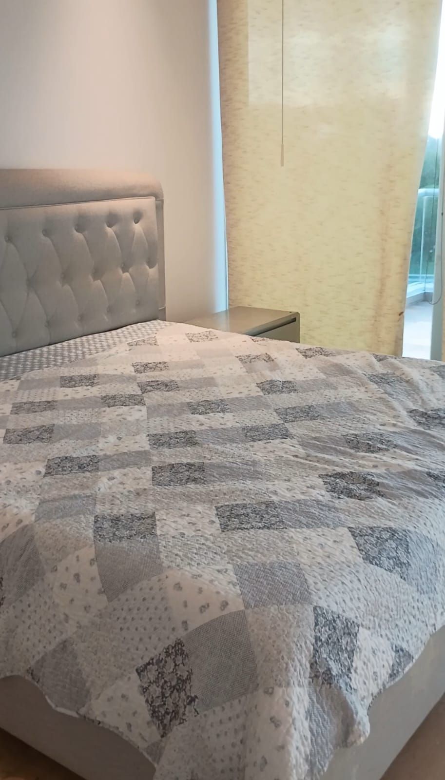 A bed with a quilt, a window, and a curtain.