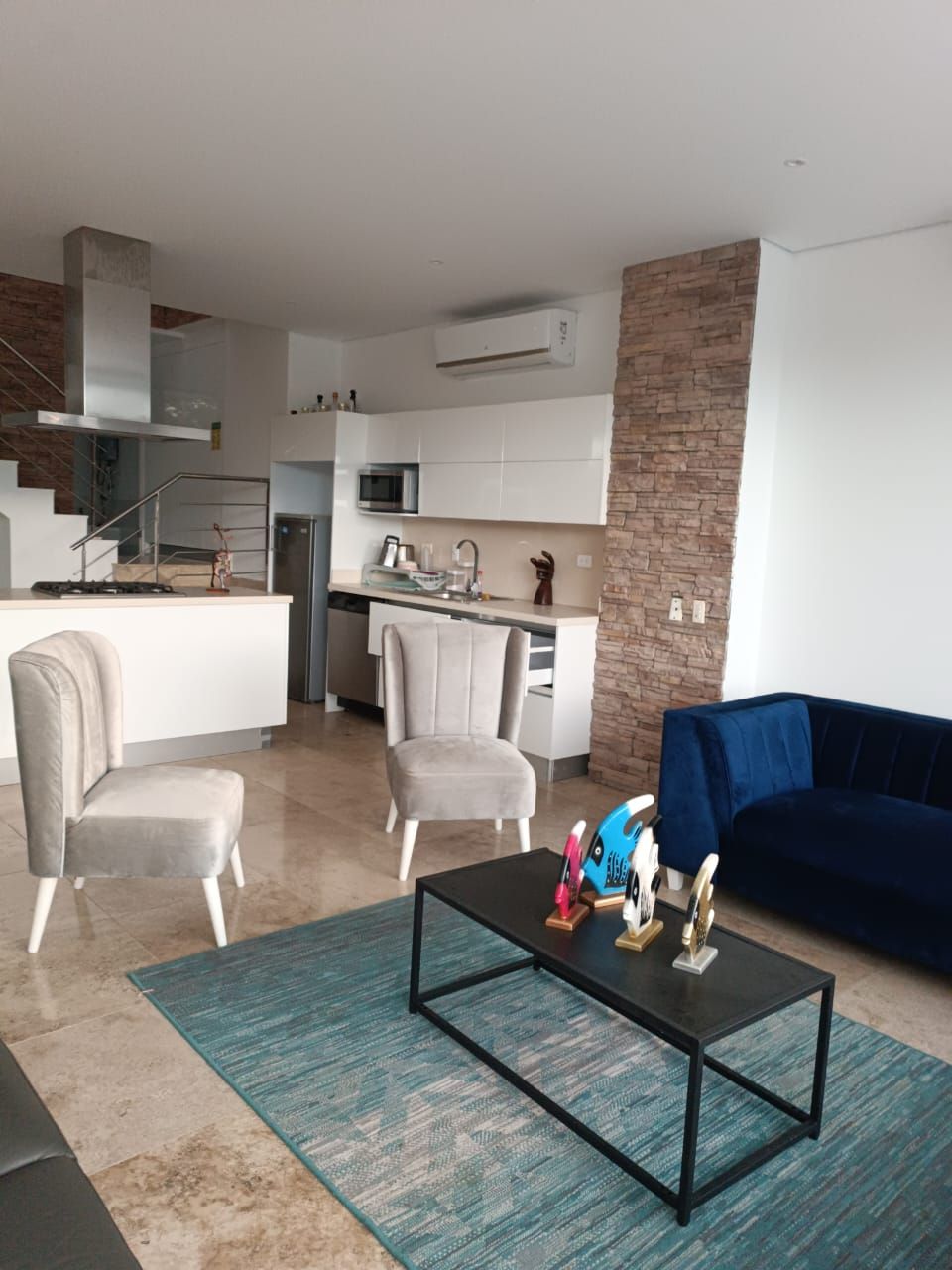 A modern living room with a sofa, two armchairs, a coffee table, and a kitchen in the background.