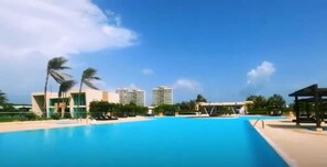 A large swimming pool with a clear blue sky and palm trees. - Agua Marina Beach Resort (Juan de Acosta)