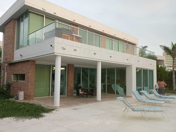 A modern building with a covered outdoor area, glass doors, and lounge chairs.