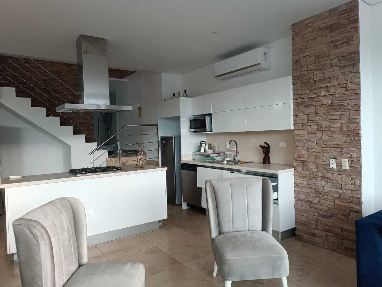 A modern kitchen with a central island, a built-in stove, and a microwave. There is a staircase leading to an upper level.