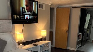 Hotellihuone, jossa on sänky, seinälle asennettu televisio, kaksi yöpöytälamppua, yöpöytä ja ovi, joka johtaa kylpyhuoneeseen.