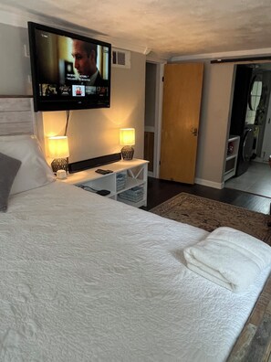 Une chambre d’hôtel comprenant un lit, un téléviseur fixé au mur, deux lampes de chevet, une table de chevet et une porte donnant accès à une salle de bain.