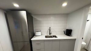 Una cucina compatta con un frigorifero in acciaio inossidabile, un piano di lavoro bianco, un lavello e una macchina da caffè.