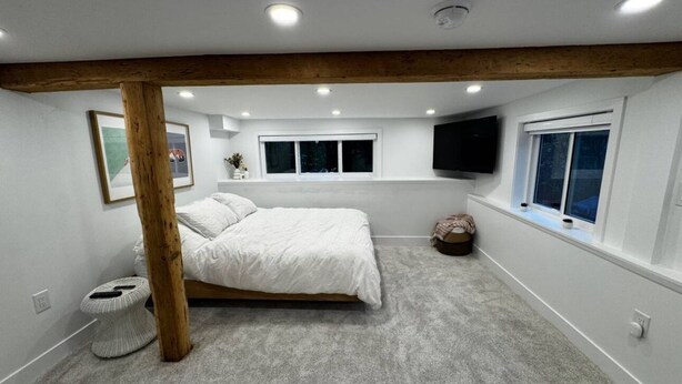 Una camera da letto con un letto, una finestra, una TV a parete e un soffitto con travi in legno.