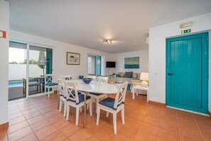 Un espacio de comedor con una mesa y sillas, un sofá, un televisor y una puerta con señal de salida.