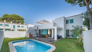 Una casa moderna con piscina, un patio con mobiliario exterior y una escalera que conduce al piso superior.