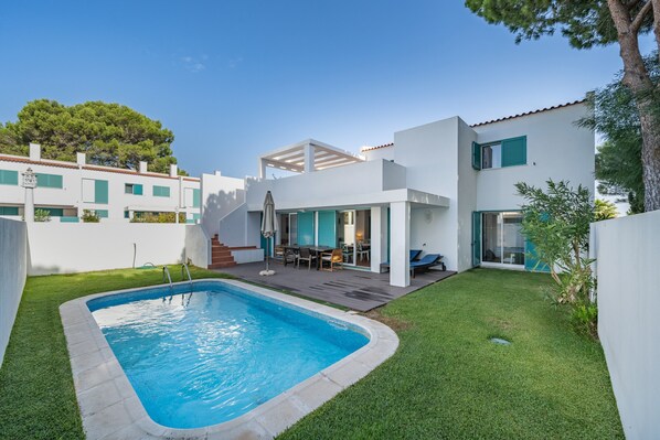 A modern house with a swimming pool, a patio with outdoor furniture, and a staircase leading to the upper floor.
