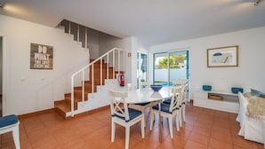 Un interior moderno con una escalera, comedor y vistas a través de puertas de cristal.