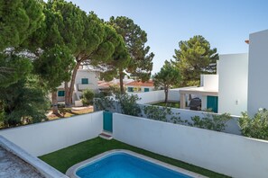 A modern building with a swimming pool, surrounded by trees and a white wall.