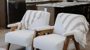 A modern kitchen with wooden cabinets, a stainless steel refrigerator, and a marble countertop. There are two white armchairs with wooden legs and a striped throw blanket. - Freedom Quarters

~Farm Setting~ (Fordland)