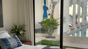 A bedroom with a large bed, a nightstand, a vase with flowers, and a view of an outdoor area with a statue and greenery. - Hotel Boutique Casa Roma (La Union)