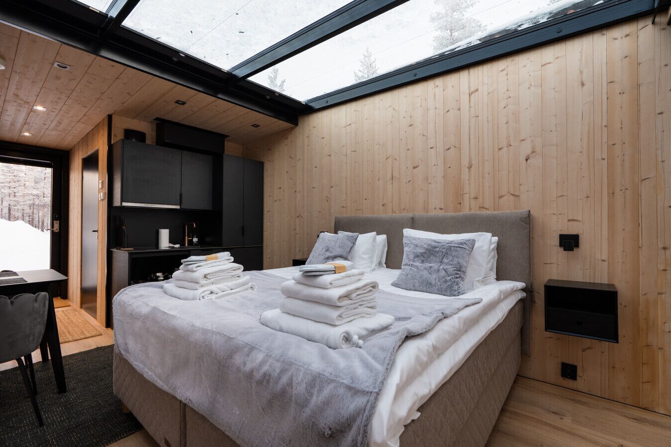 A modern bedroom with a large bed, a desk, and a view through a skylight.