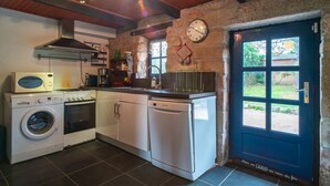Een kleine keuken met een wasmachine, oven en vaatwasser, een klok aan de muur, en een deur met een raam.