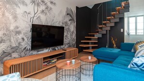 A modern living room with a large flat-screen TV, a blue sofa, two round coffee tables, and a unique wooden staircase.