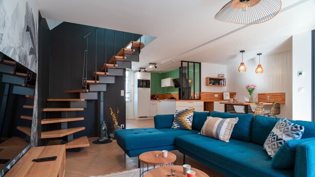 A modern living room with a blue sofa, wooden coffee table, and a staircase with wooden steps.