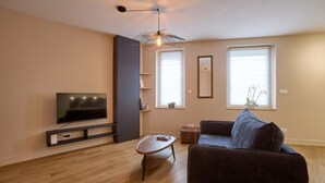 Ein modernes Wohnzimmer mit Flachbildfernseher, einem dunklen Sofa, einem Couchtisch und einer außergewöhnlichen Deckenleuchte.