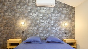 Ein Schlafzimmer mit gemustertem Wandpapier, zwei Nachttischen und einem Bett mit blauer Bettwäsche.