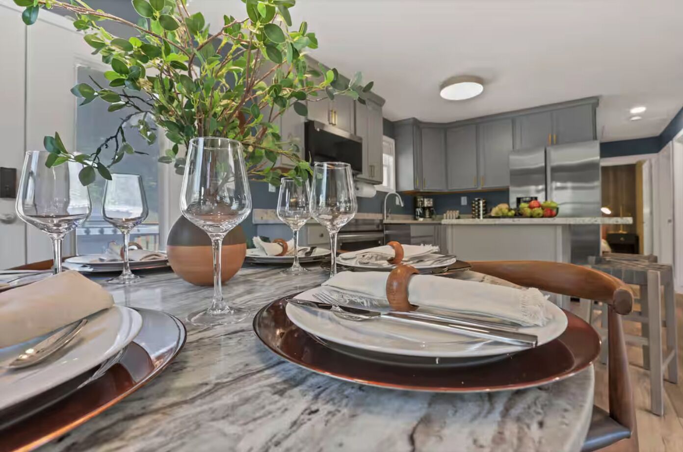 A modern dining area with a marble table, wine glasses, and a potted plant.