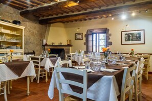 Un espace repas avec des tables dressées, des murs en pierre, des poutres en bois et une cheminée.