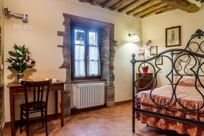 Ein Schlafzimmer mit Bett, Schreibtisch mit Stuhl, Heizkörper, einem Fenster mit Vorhängen und einer Wandlampe.