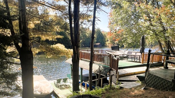 A lakeside deck with outdoor seating and a fire pit. - ADK Channel House - Spacious, waterfront home. Huge boathouse with top sun deck (Old Forge)