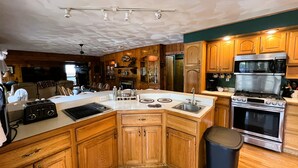 A kitchen with wooden cabinets, a stainless steel stove, and a microwave. - ADK Channel House - Spacious, waterfront home. Huge boathouse with top sun deck (Old Forge)