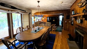 A dining area with a wooden table and chairs, a chandelier, and a fireplace. - ADK Channel House - Spacious, waterfront home. Huge boathouse with top sun deck (Old Forge)
