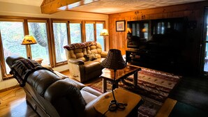 A cozy living room with a leather sofa, a cushioned chair, a television, and a fireplace. - ADK Channel House - Spacious, waterfront home. Huge boathouse with top sun deck (Old Forge)