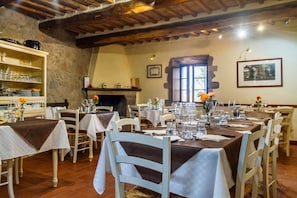 Comedor con mesas dispuestas para el servicio, paredes de piedra, vigas de madera y una chimenea.