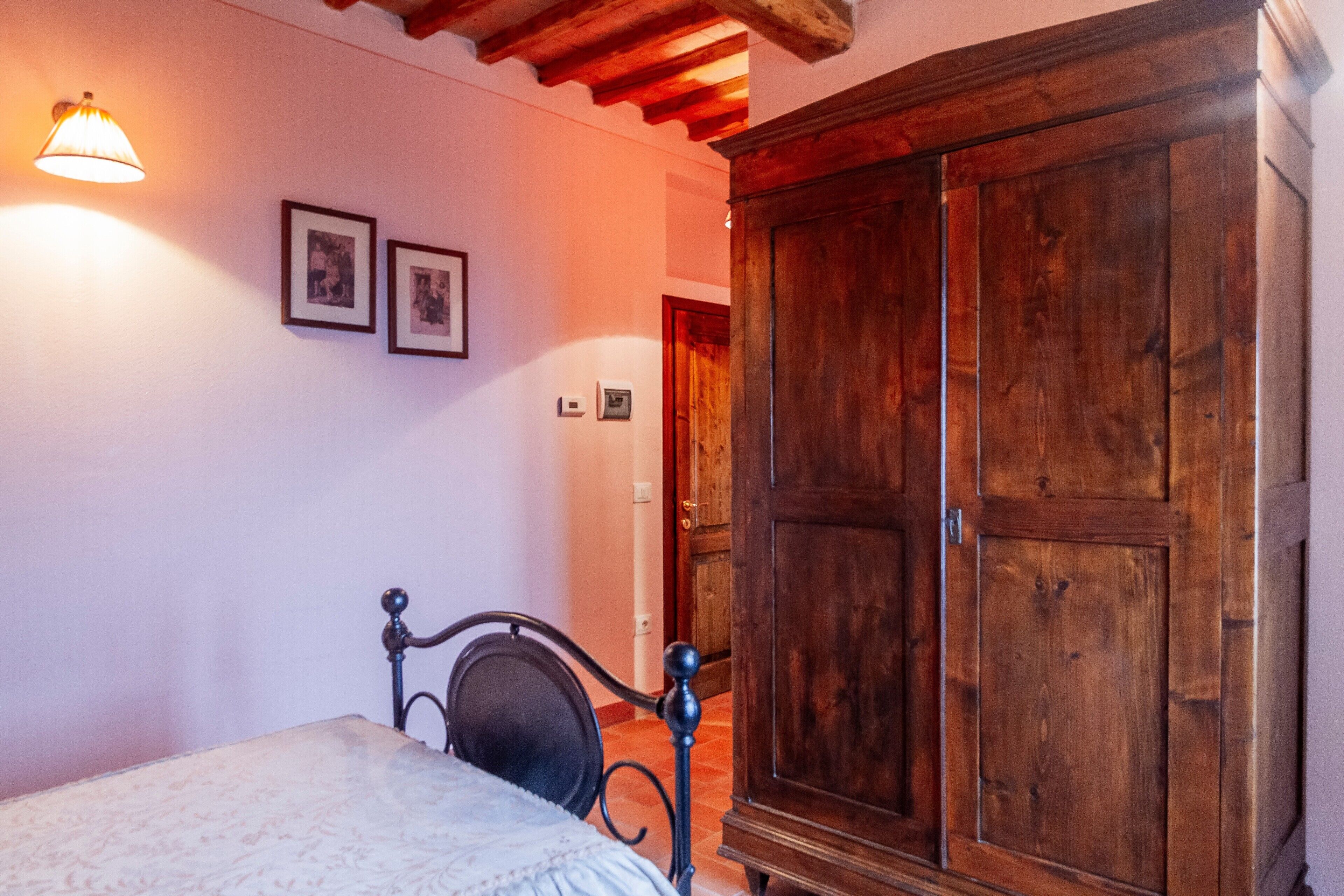 A bedroom with a bed, wooden wardrobe, and wall-mounted light fixture.