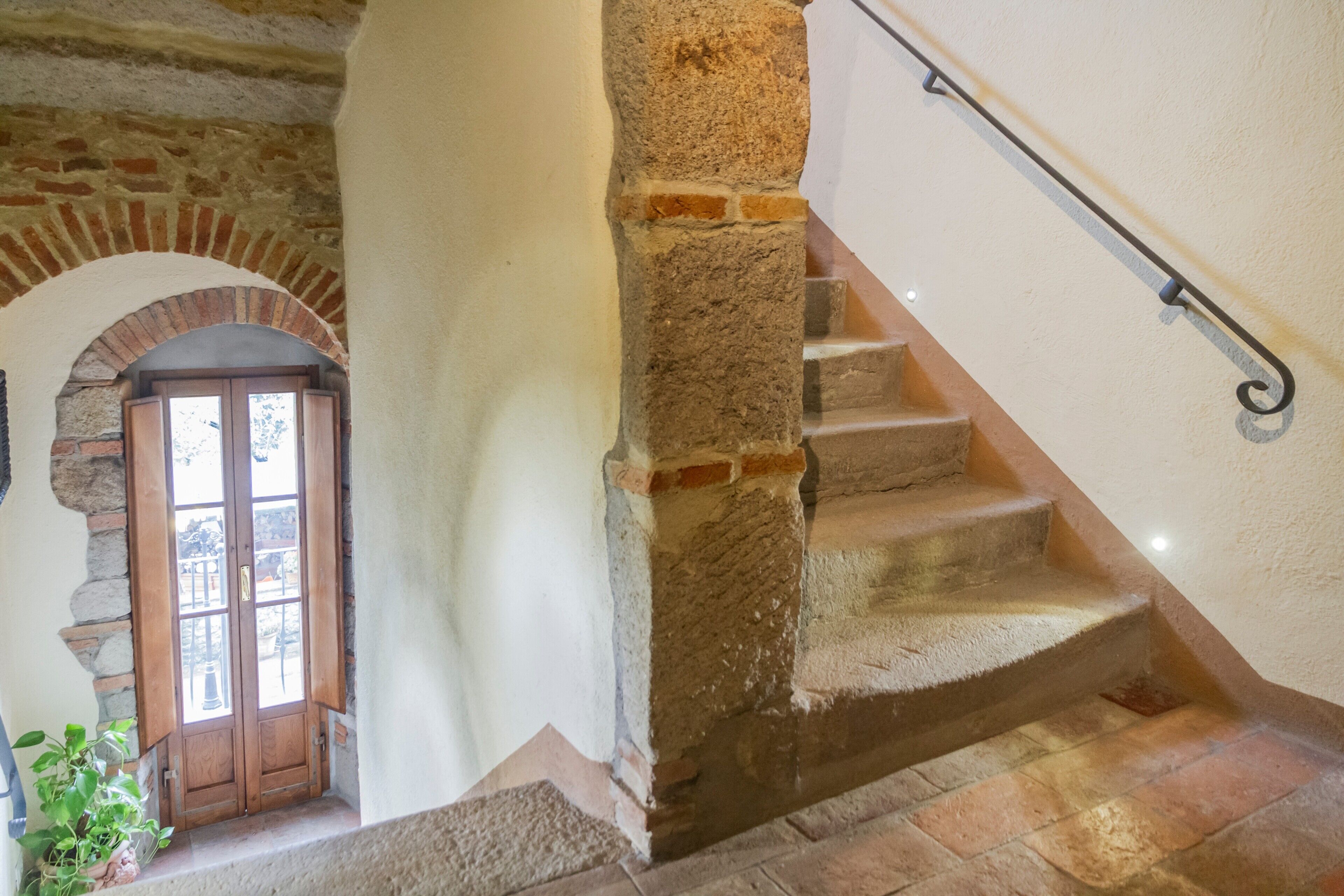 A stone staircase with a metal handrail, a wooden door with glass panels, and a stone archway.