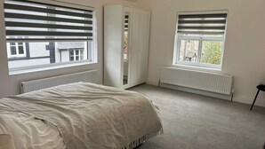Une chambre à coucher avec un lit, deux fenêtres équipées de stores, une armoire et un radiateur.