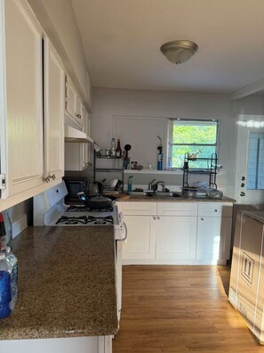 Une cuisine avec des meubles blancs, un plan de travail en granit, une cuisinière et une fenêtre donnant sur un paysage verdoyant.